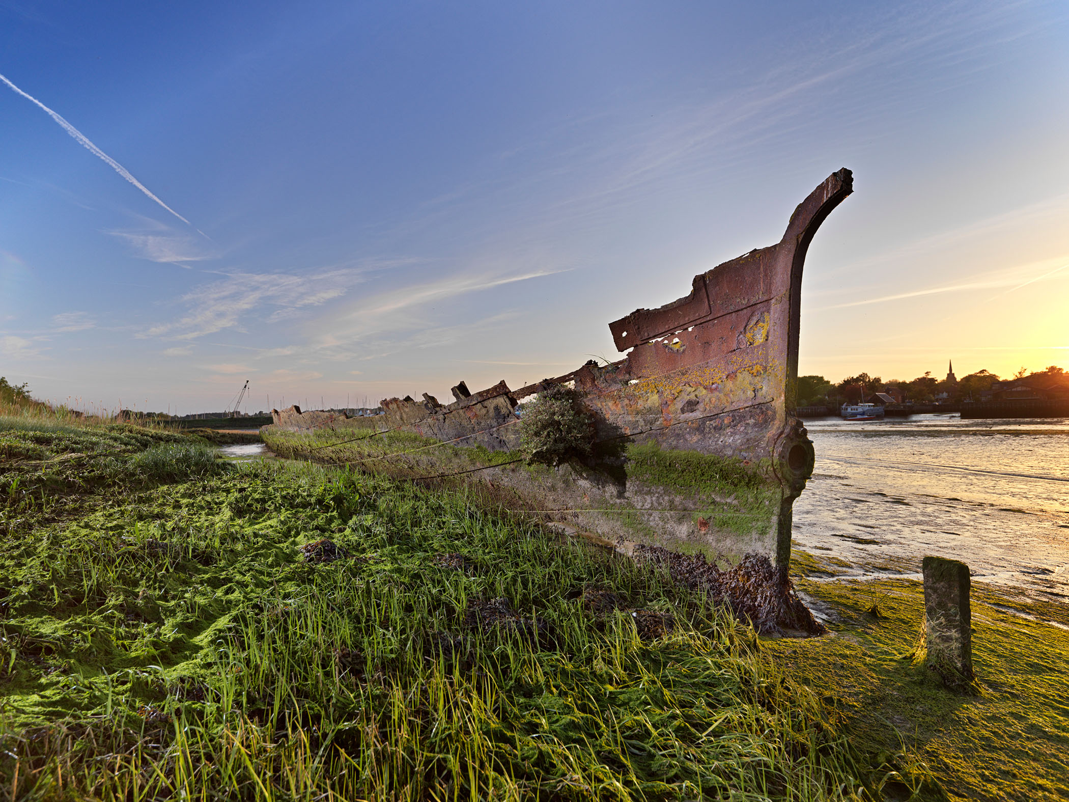The remains of a ship on a grassy river bank.