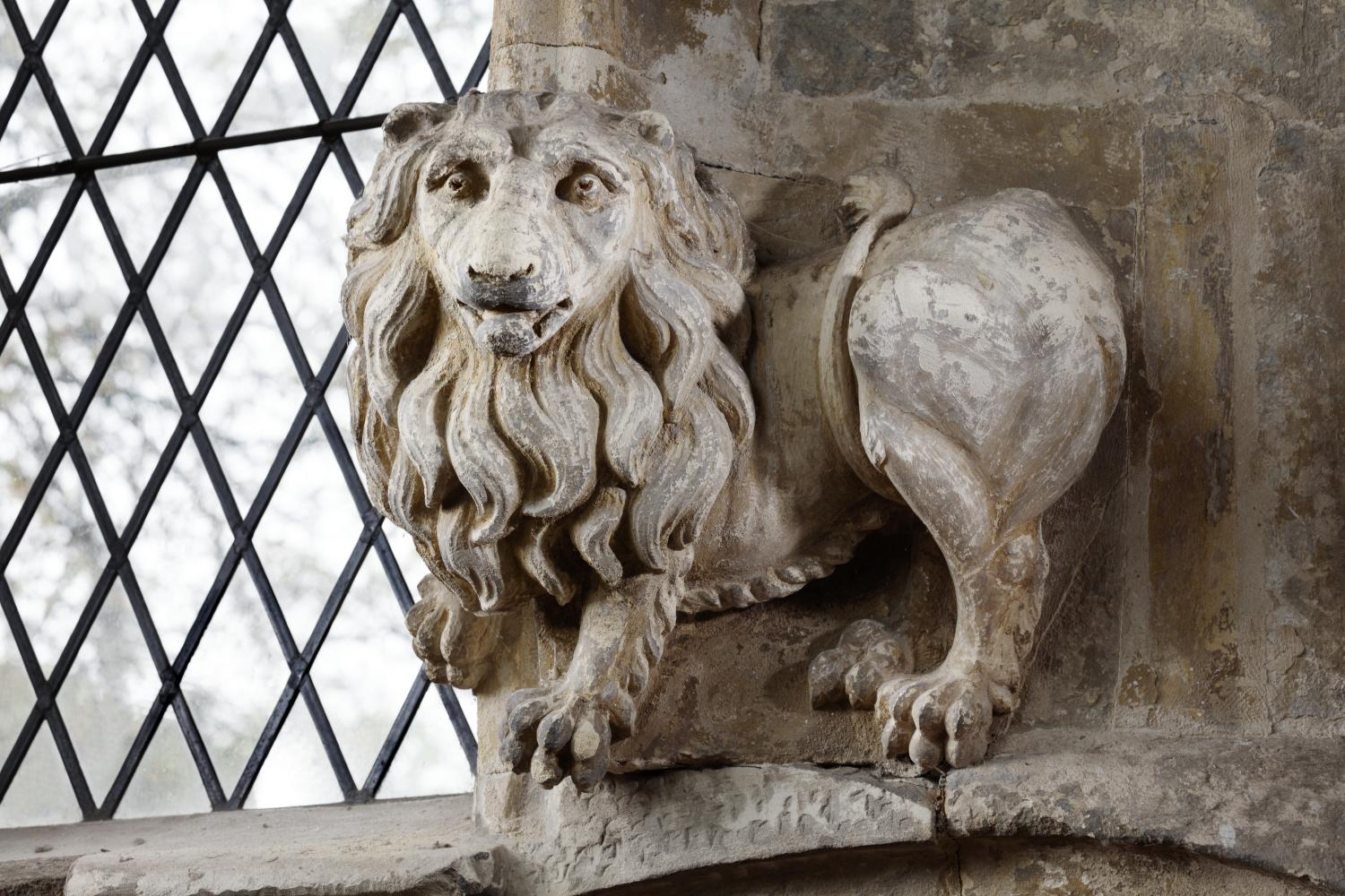Stone carving of a lion on an interior wall next to a leaded window.