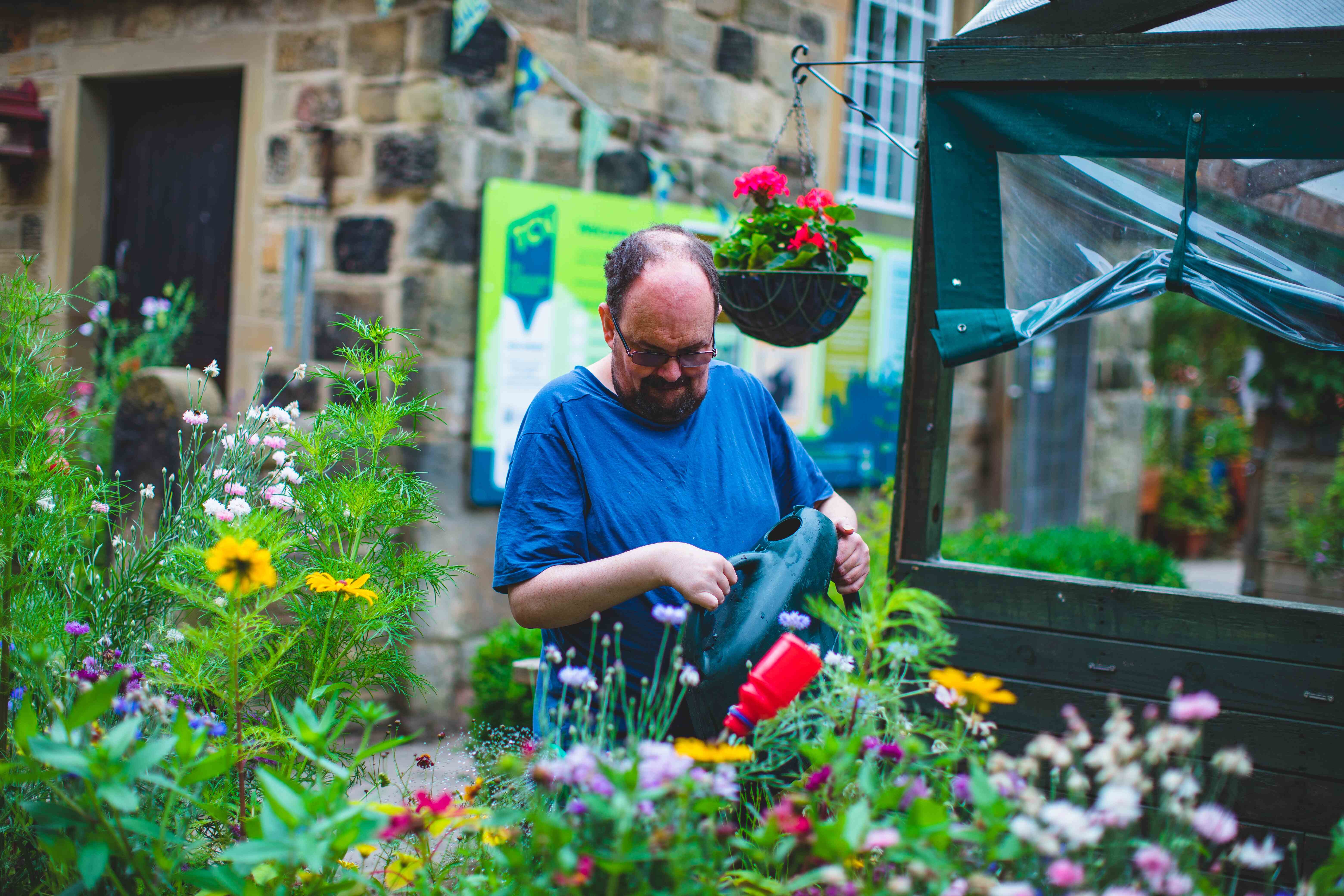 A man in a blue t-shirt watering garden plants with a green watering can