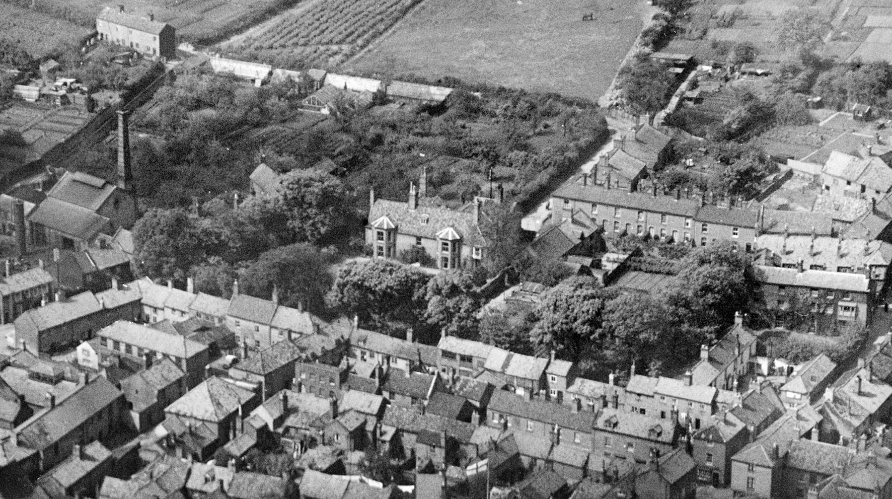 A black and white images shows the centre of North Walsham. Focused on a grand house, it also shows tightly packed streets of houses around it and fields to the north.