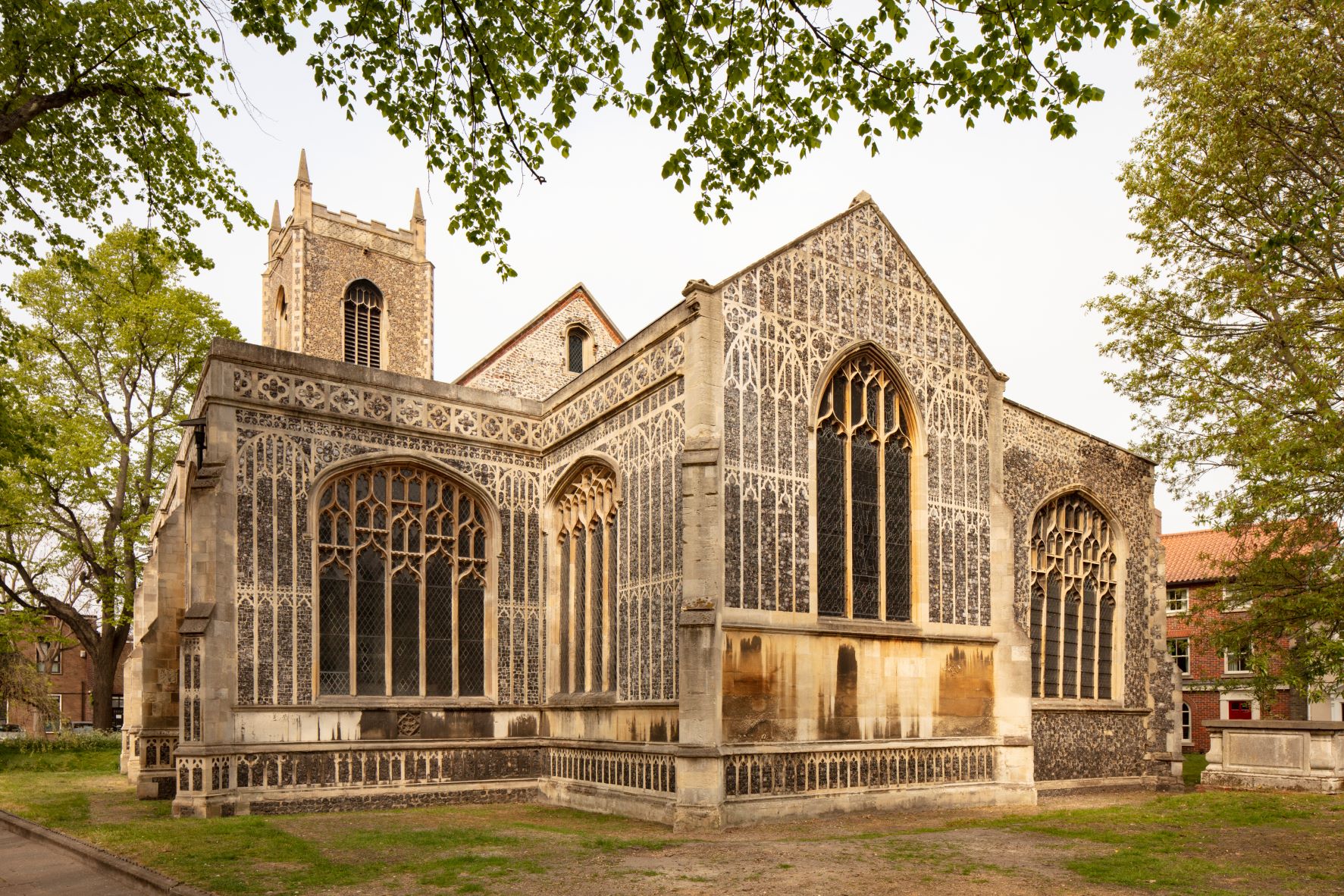 the image shows the front of the church, with its ornate brickwork and large arched windows. The church tower can be seen behind.