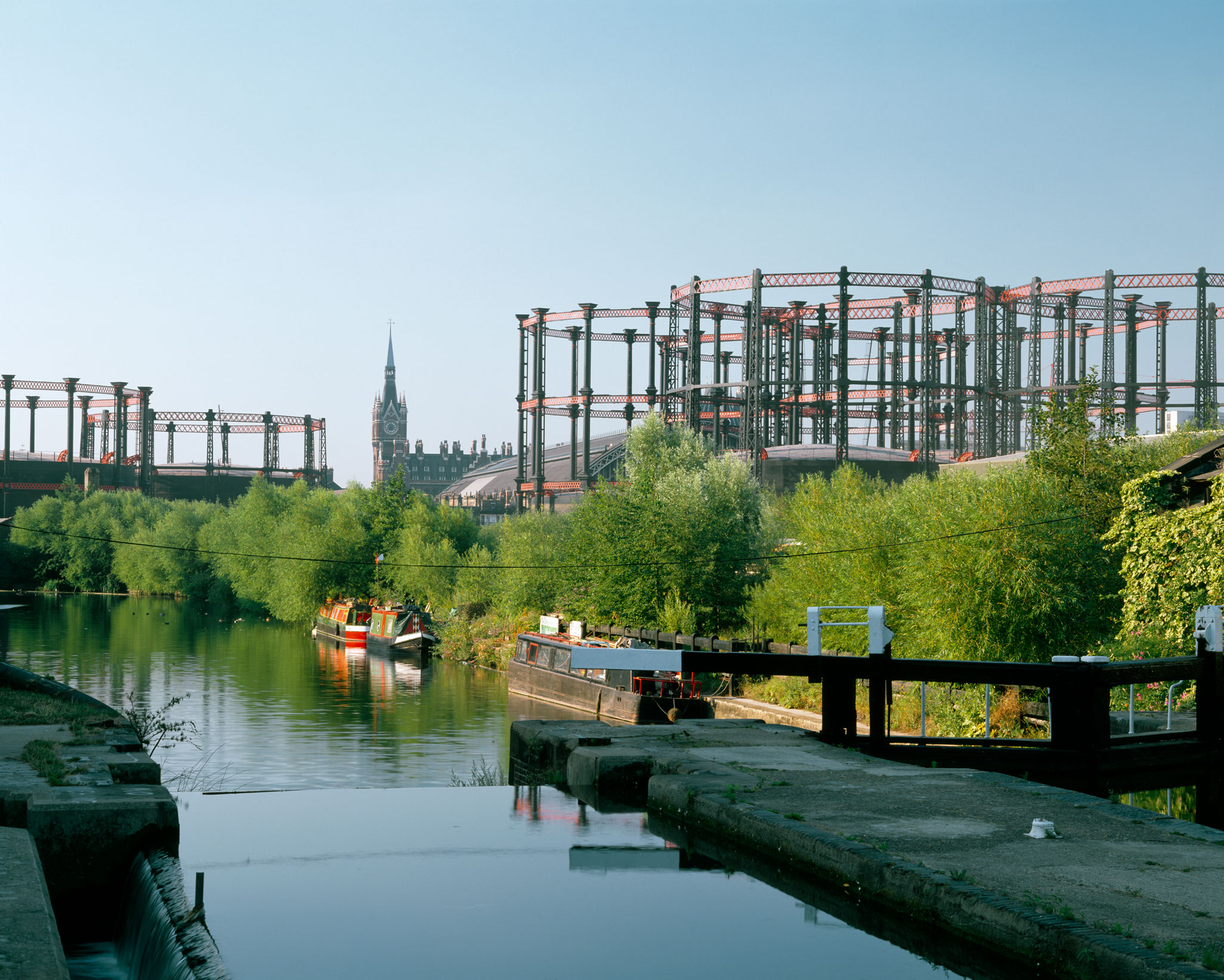 Gasholders next to an urban canal with a railway station in the background.