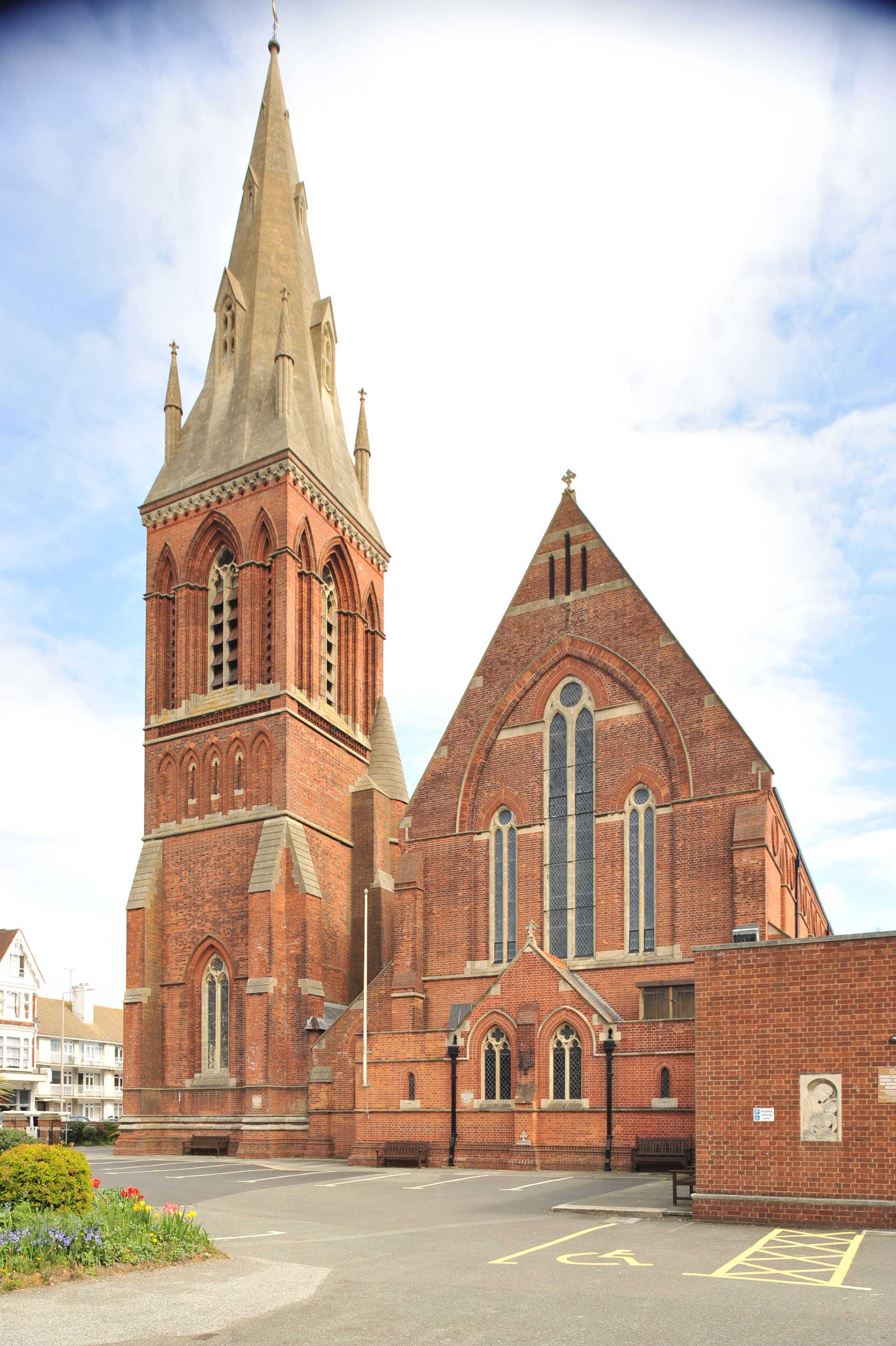 Red brick church with stone highlights and a stone spire with small windows.