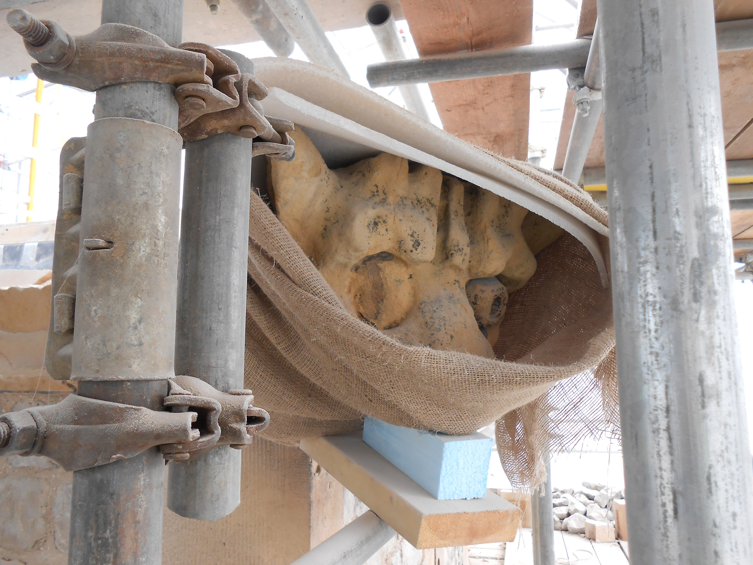 A stone carving wrapped in foam and cloth, surrounded by scaffolding.