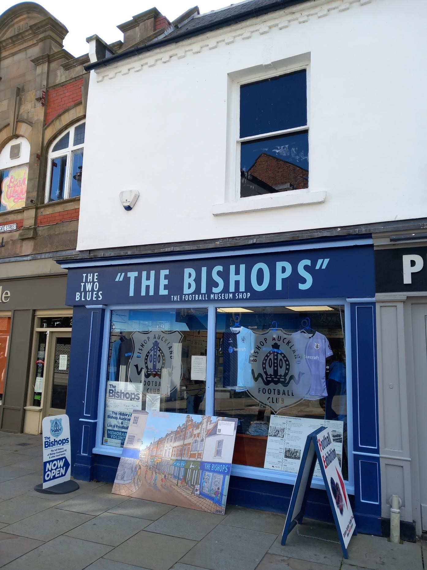 The Bishops shopfront with signs on the window advertising Bishop Auckland Football Club and the football exhibition inside 