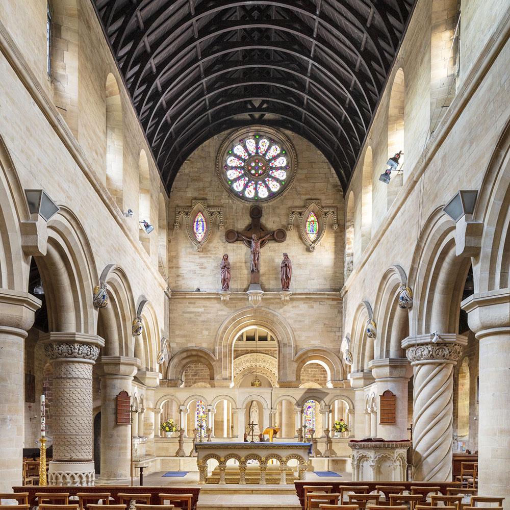 Interior of the Church of St Edward, with a nave flanked by ornate columns, and complex stained glass window rose. 