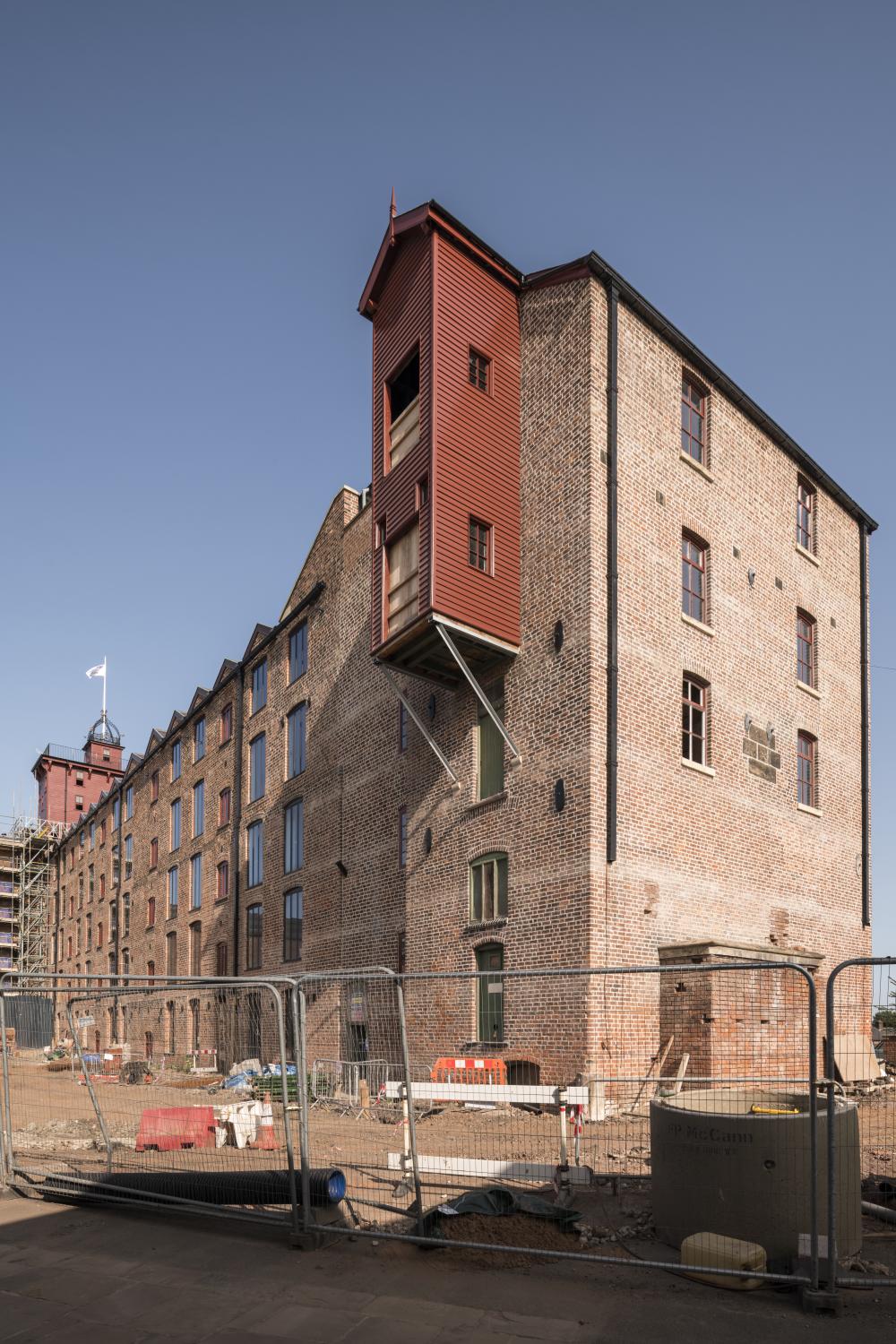 A five storey brick warehouse type building with security fencing and building materials in the foreground.