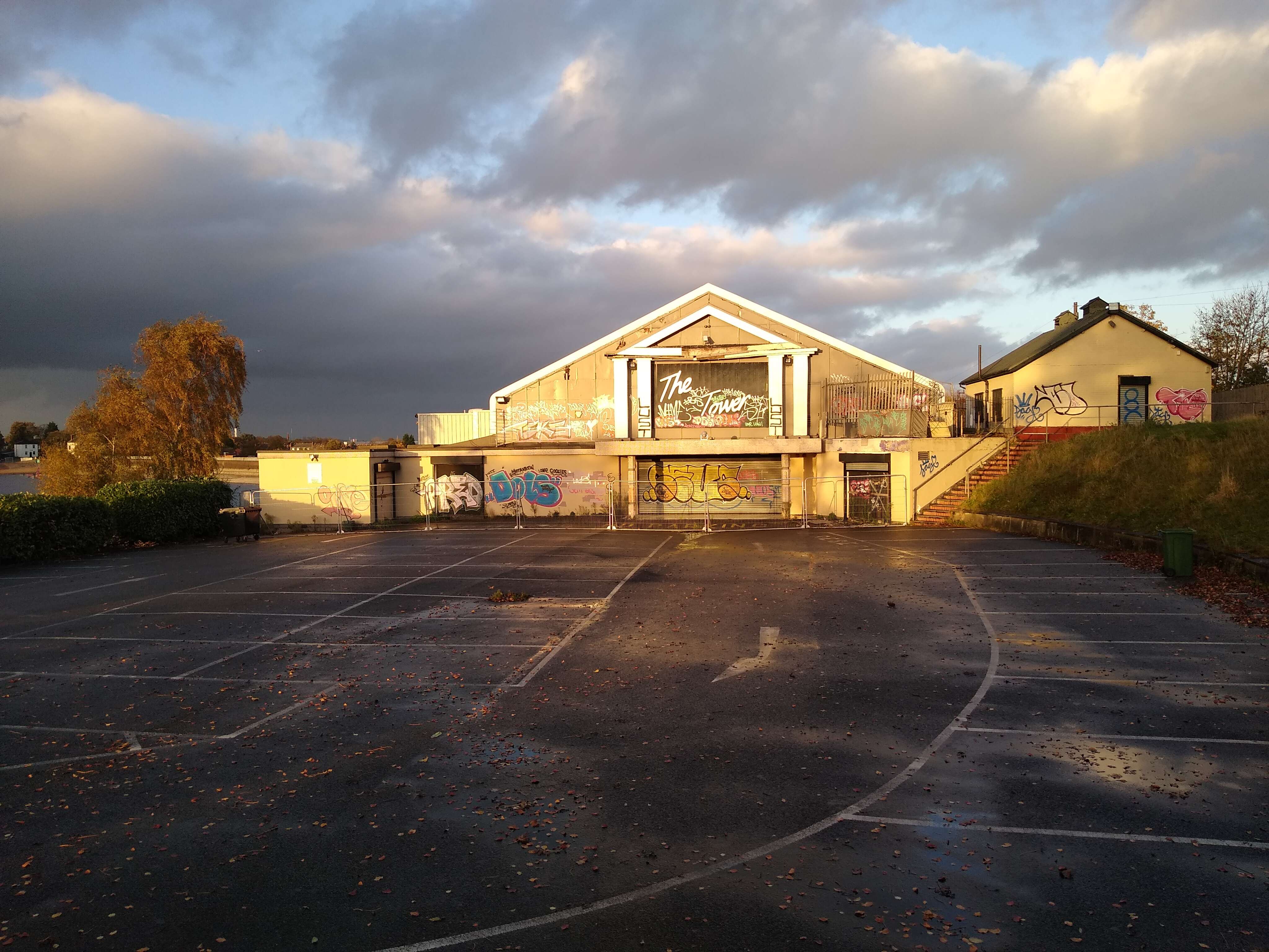A building with graffiti in the evening light. An empty tarmac car park is in the foreground.