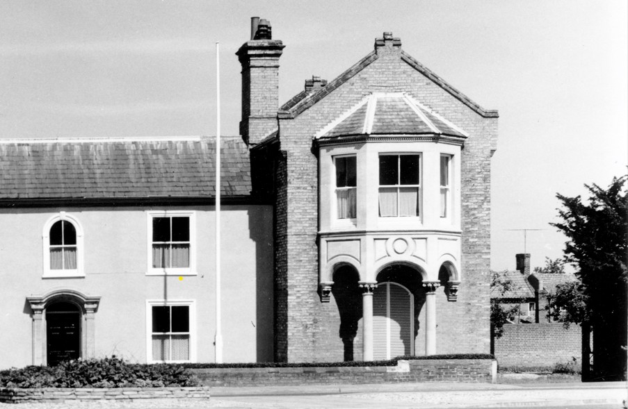 A black and white photo of The Cedars shows a two storey brick building with pillared doorway, and a sculptured bay window with pillars on a projected storey to the right.